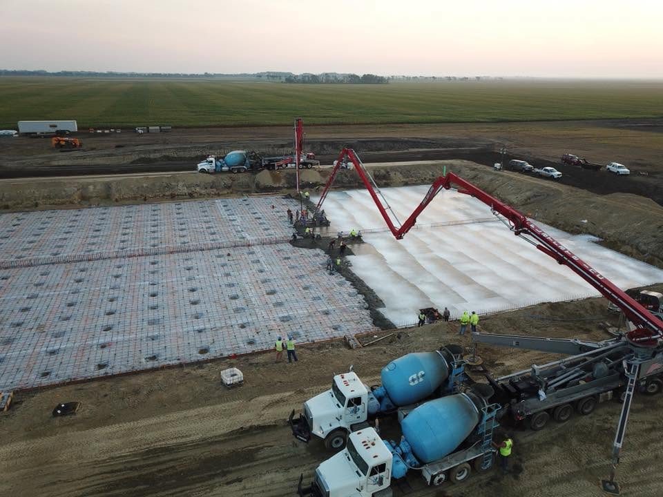 Aerial sunrise view of a commercial slab pour with two mixer trucks and a pump truck